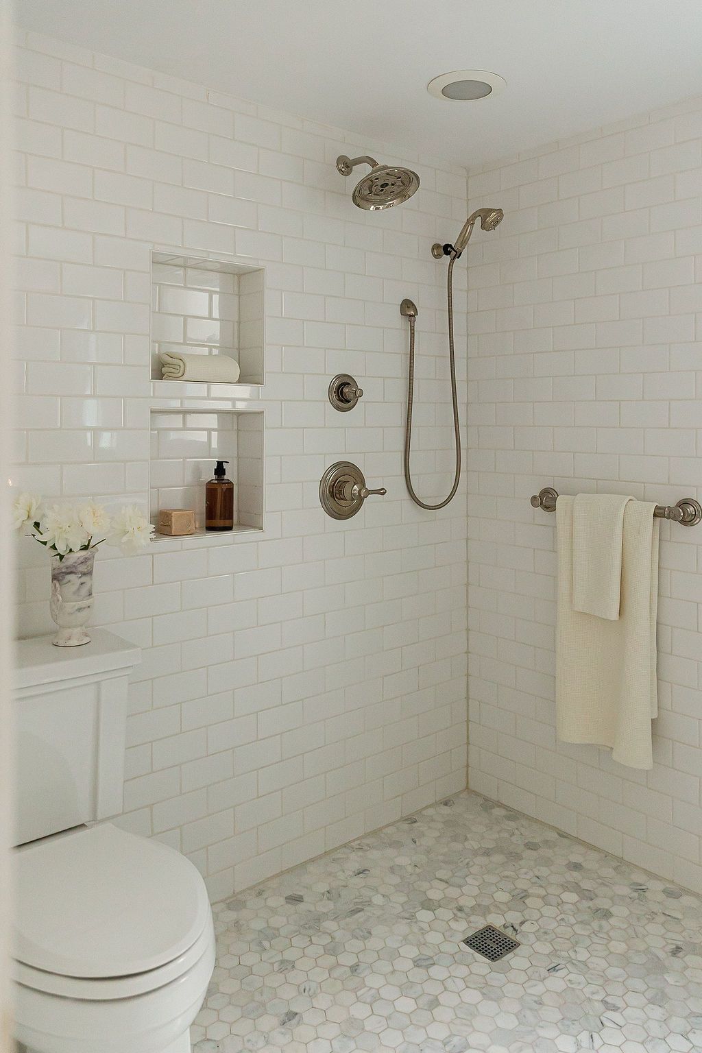 Elegant white bathroom with subway tile walls, marble hexagon floor tiles, and built-in shower niches featuring modern fixtures.