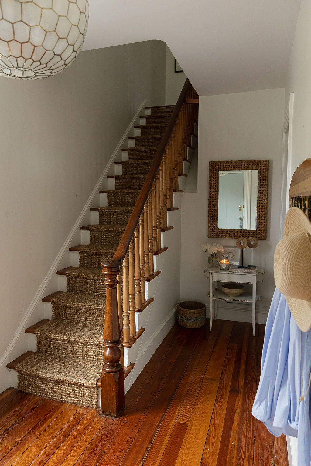 A carpeted staircase with wooden railing leads upstairs in a cozy entryway featuring hardwood floors and a decorative mirror.