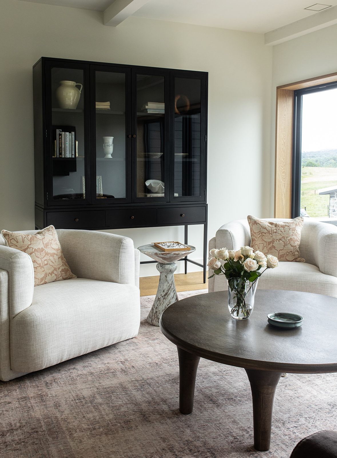 Elegant sitting room with cream bouclé chairs, round dark wood coffee table, and black glass display cabinet.