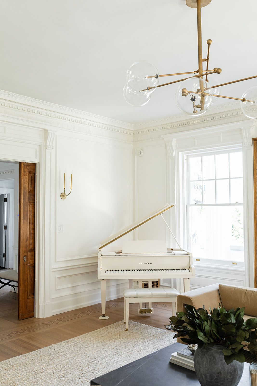 White grand piano in bright room with modern brass chandelier and crown molding.