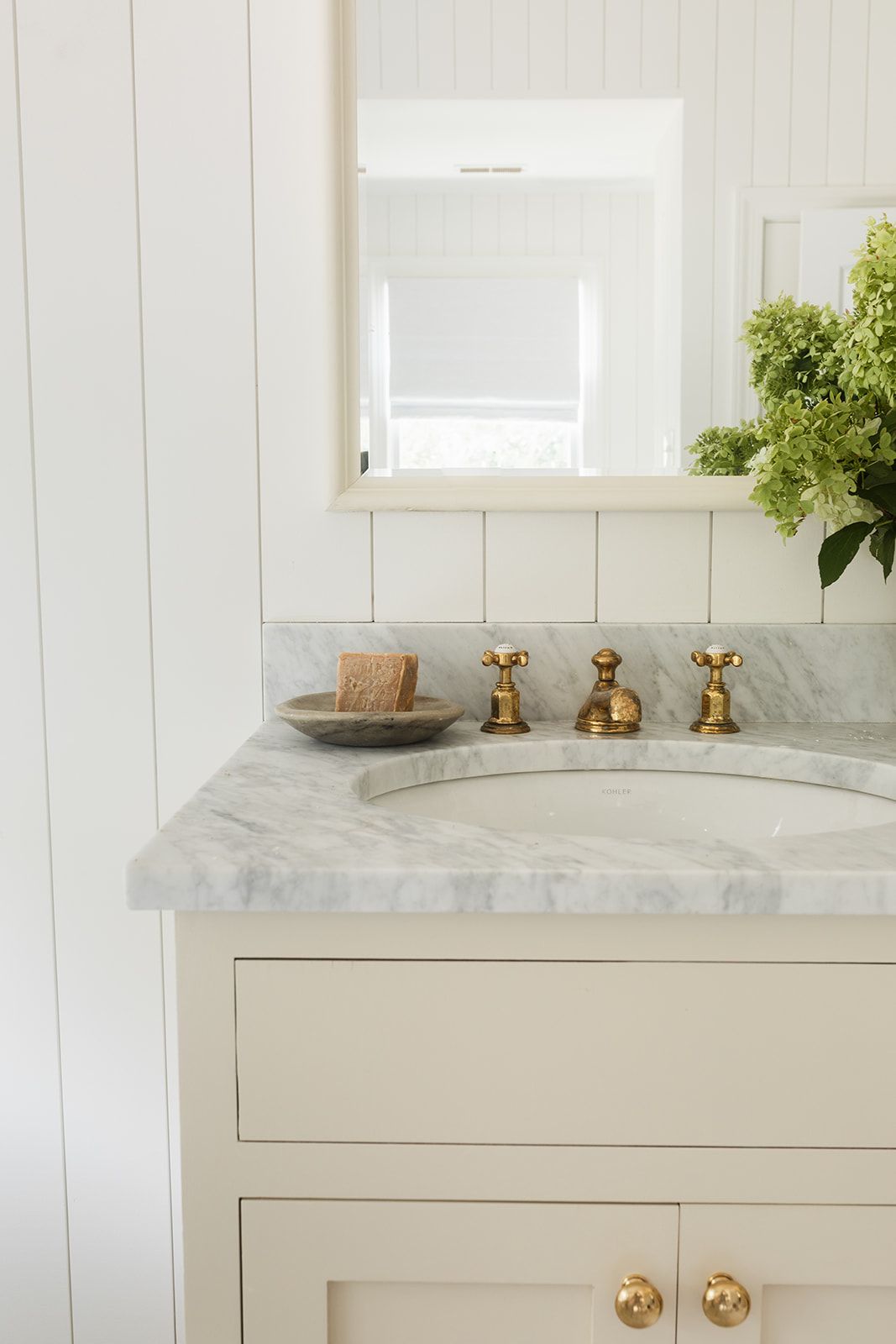 White bathroom vanity with marble countertop, brass faucet fixtures, undermount sink, and a framed mirror above.