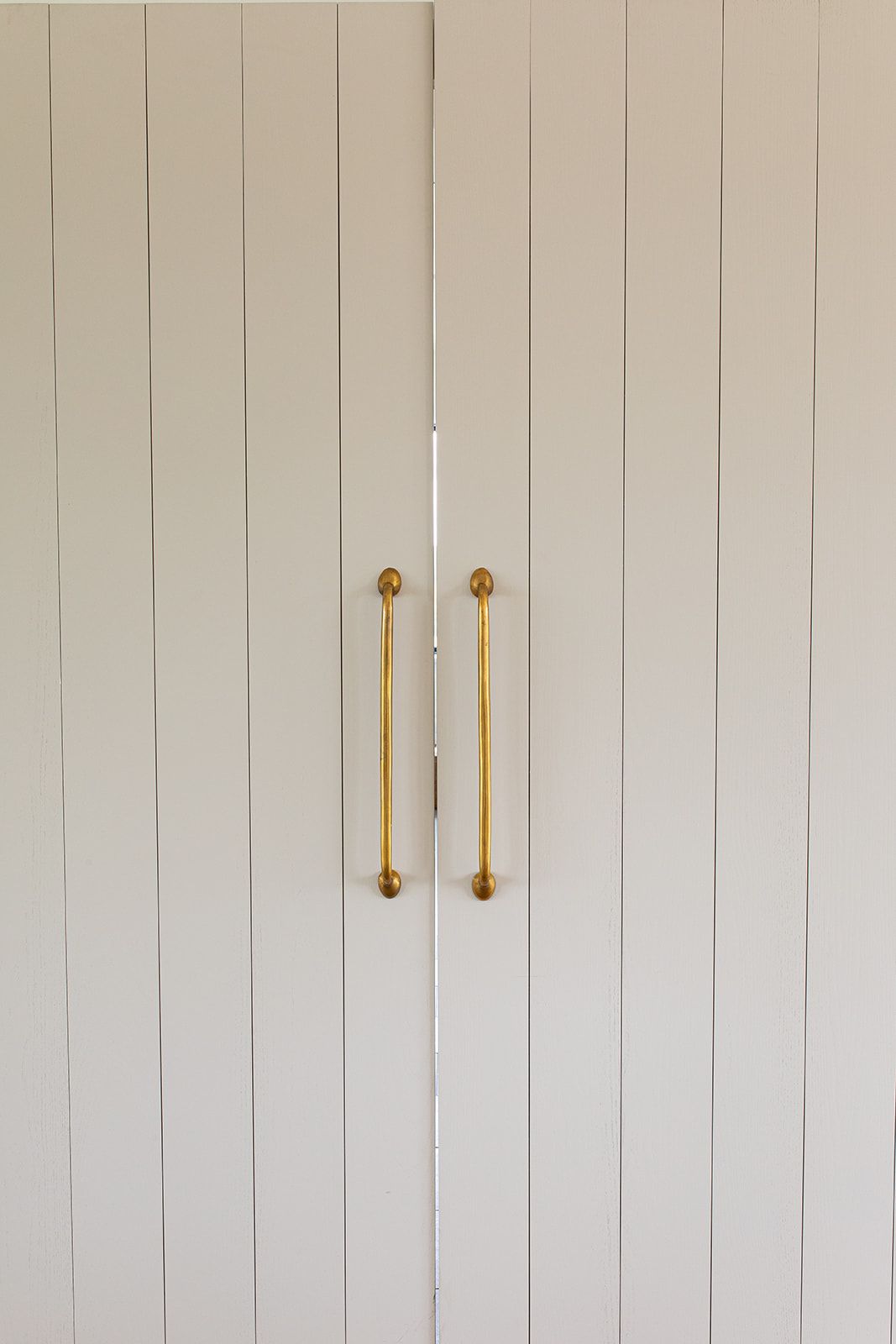 White vertical shiplap cabinet doors with elegant paired antique brass bar pulls.