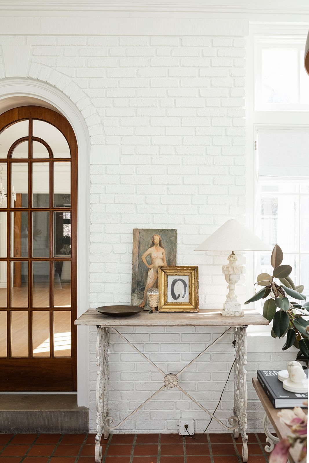 Vintage-style entryway with arched doorway, white brick walls, and antique console table with decorative items.