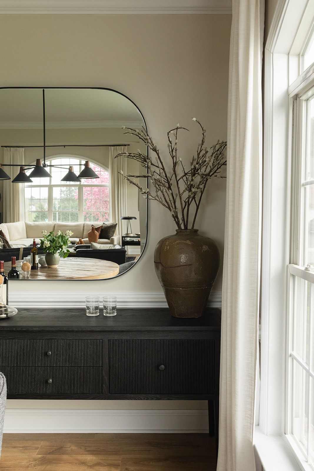 Modern interior design featuring black wooden cabinets, large windows, and decorative ceramic vase with branches on display.