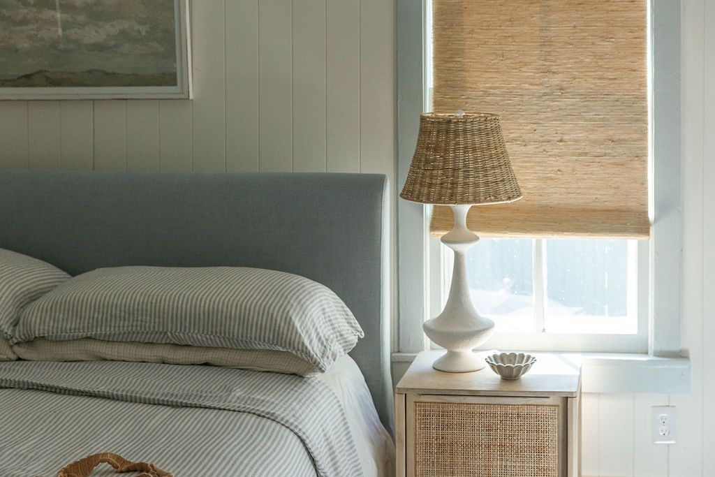 A cozy bedroom interior with natural woven bamboo shades, white bedding, and soft neutral decor elements.