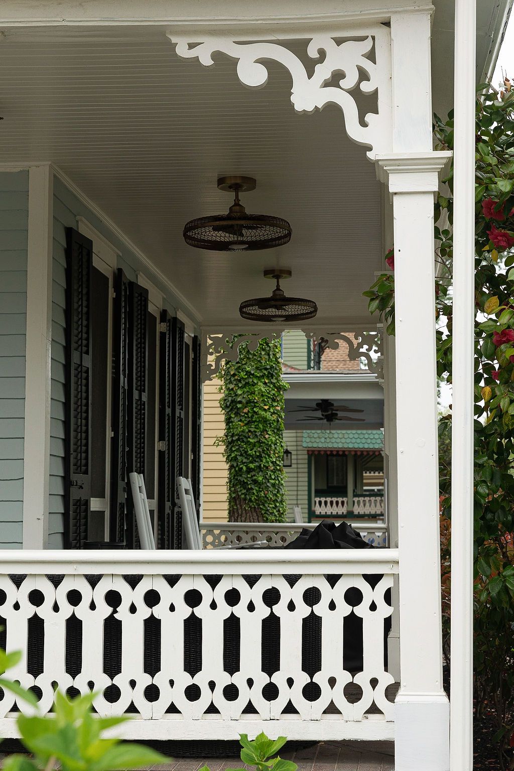 Victorian-style porch with ornate white railings, decorative brackets, and vintage fan fixtures on a mint green house.