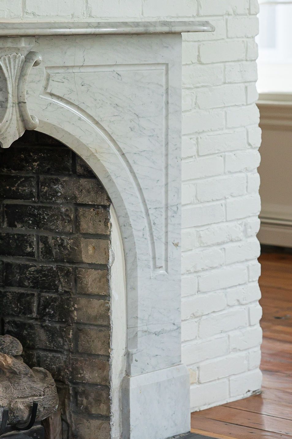 Detailed view of a white painted brick fireplace with an arched opening and dark interior cavity in a historic home.