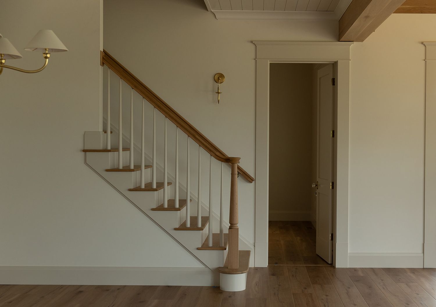 Elegant wooden staircase with white balusters and oak handrail in a bright, minimalist home interior with hardwood floors.