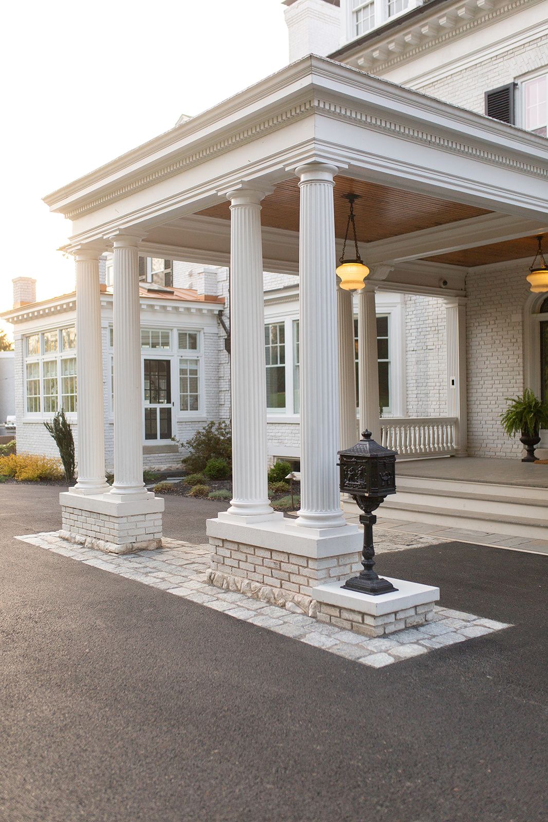 Grand entrance portico with white columns and stone bases featuring classic lamp posts.