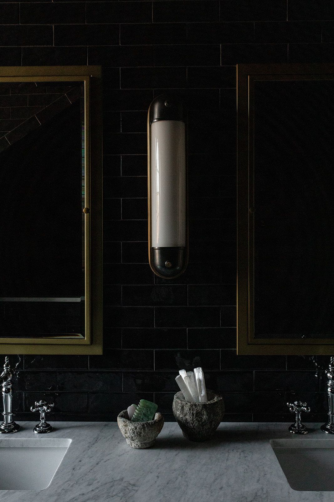 Modern bathroom vanity with dual sinks, black tile walls, and brass-framed mirrors.