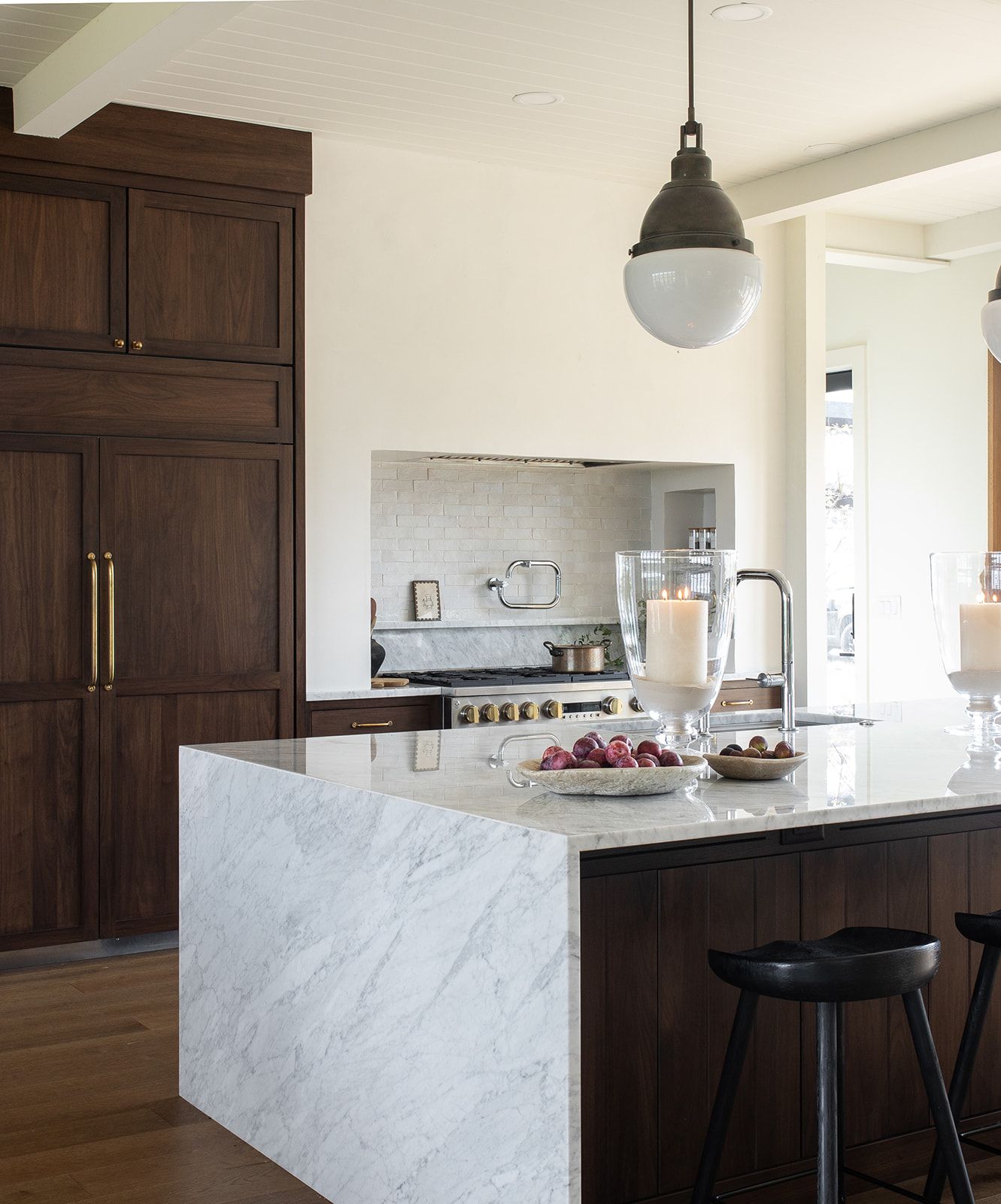 Elegant kitchen featuring dark wood cabinetry, thick marble waterfall island, globe pendant light, and black bar stools.