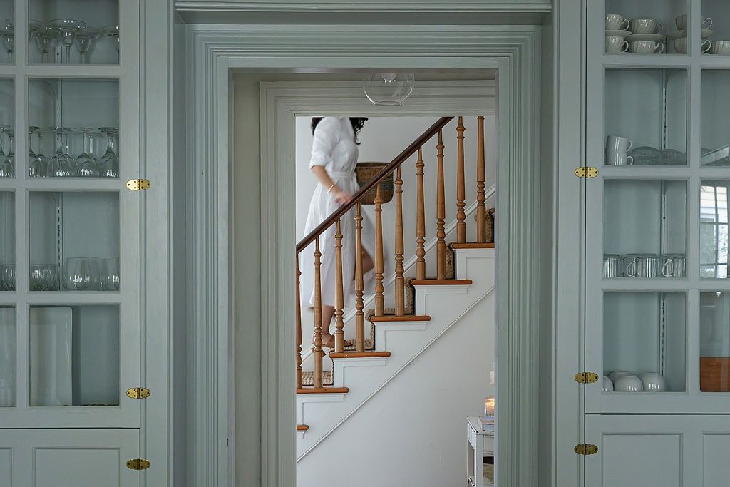 Elegant home interior with sage green built-in cabinets flanking a doorway leading to a wooden staircase.