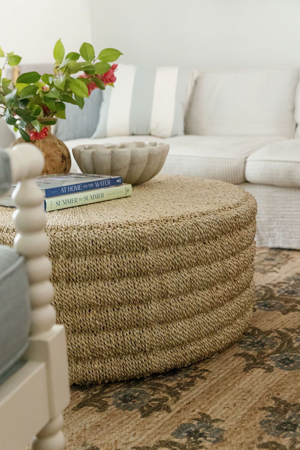 Large woven seagrass bench ottoman adds natural texture beside white sofa and traditional patterned rug in living room.