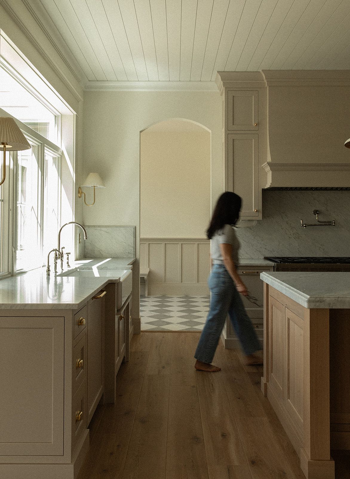 Spacious transitional kitchen with sage cabinetry, checkered floor, shiplap ceiling, brass fixtures, and marble countertops.