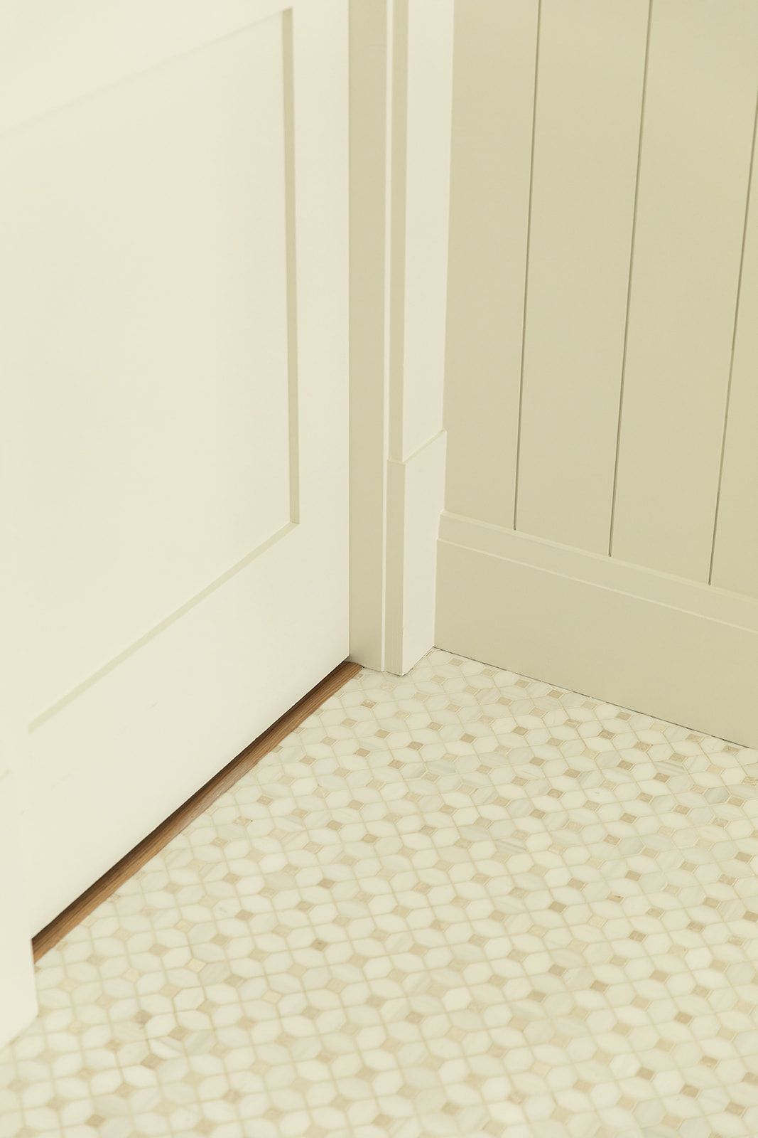 Close-up of white mosaic penny tile bathroom floor meeting white shiplap walls and a paneled door.
