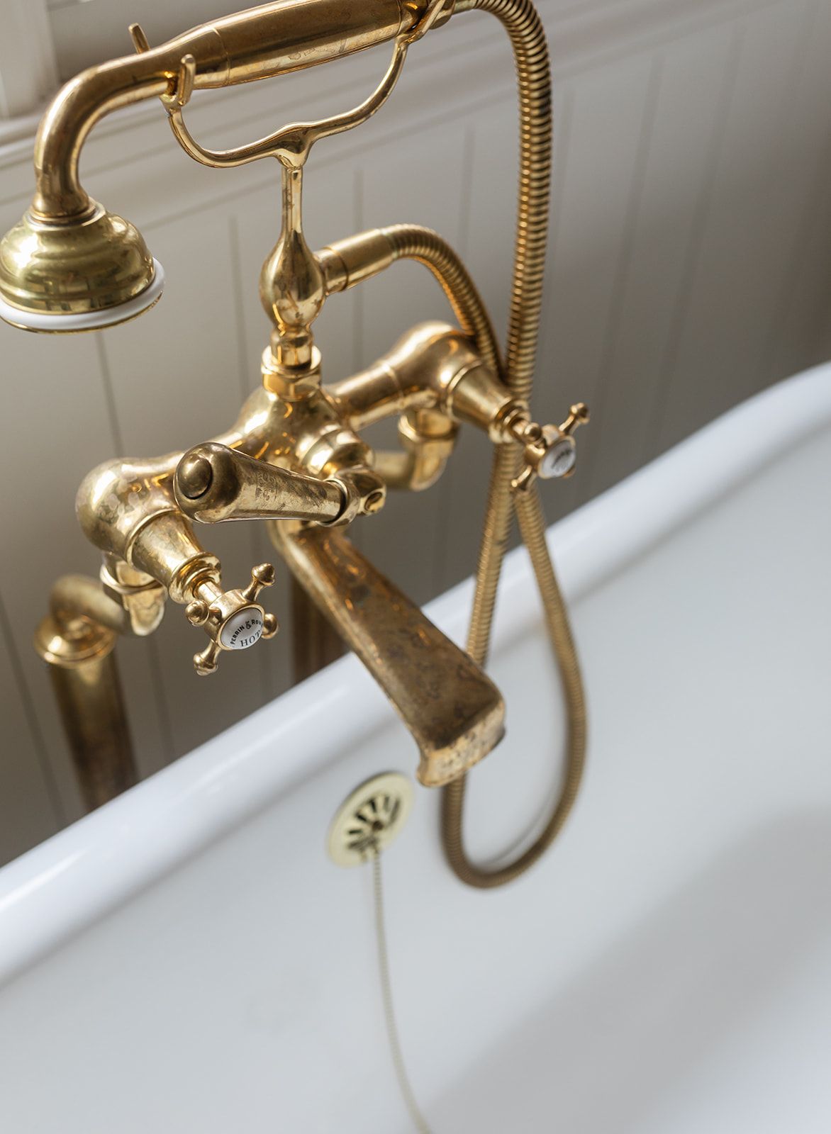 Vintage brass clawfoot bathtub faucet with cross handles and handheld shower attachment in elegant gold finish.