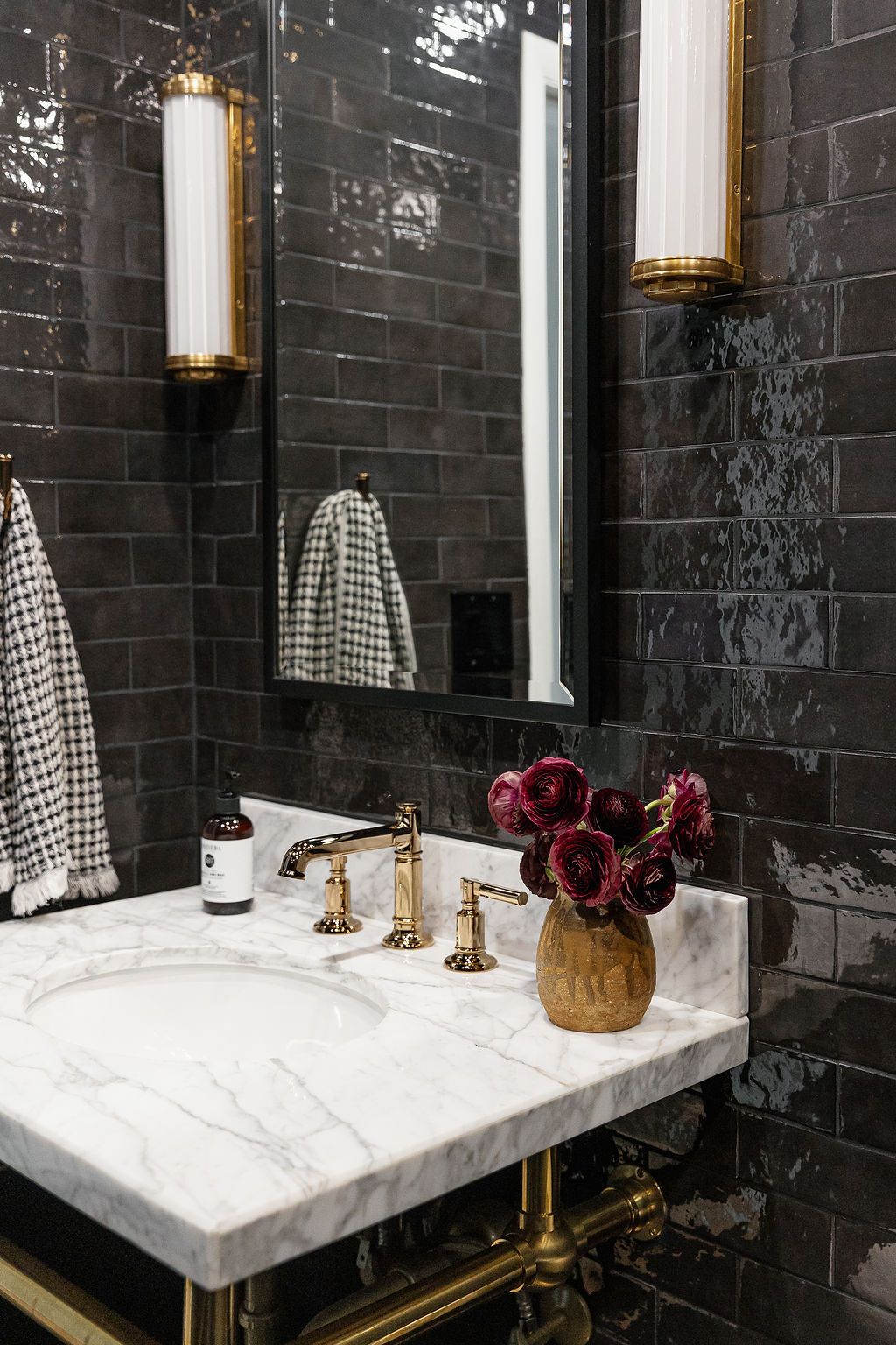 A luxurious bathroom interior with black stone walls, marble countertop, brass fixtures, and hanging pendant lights.