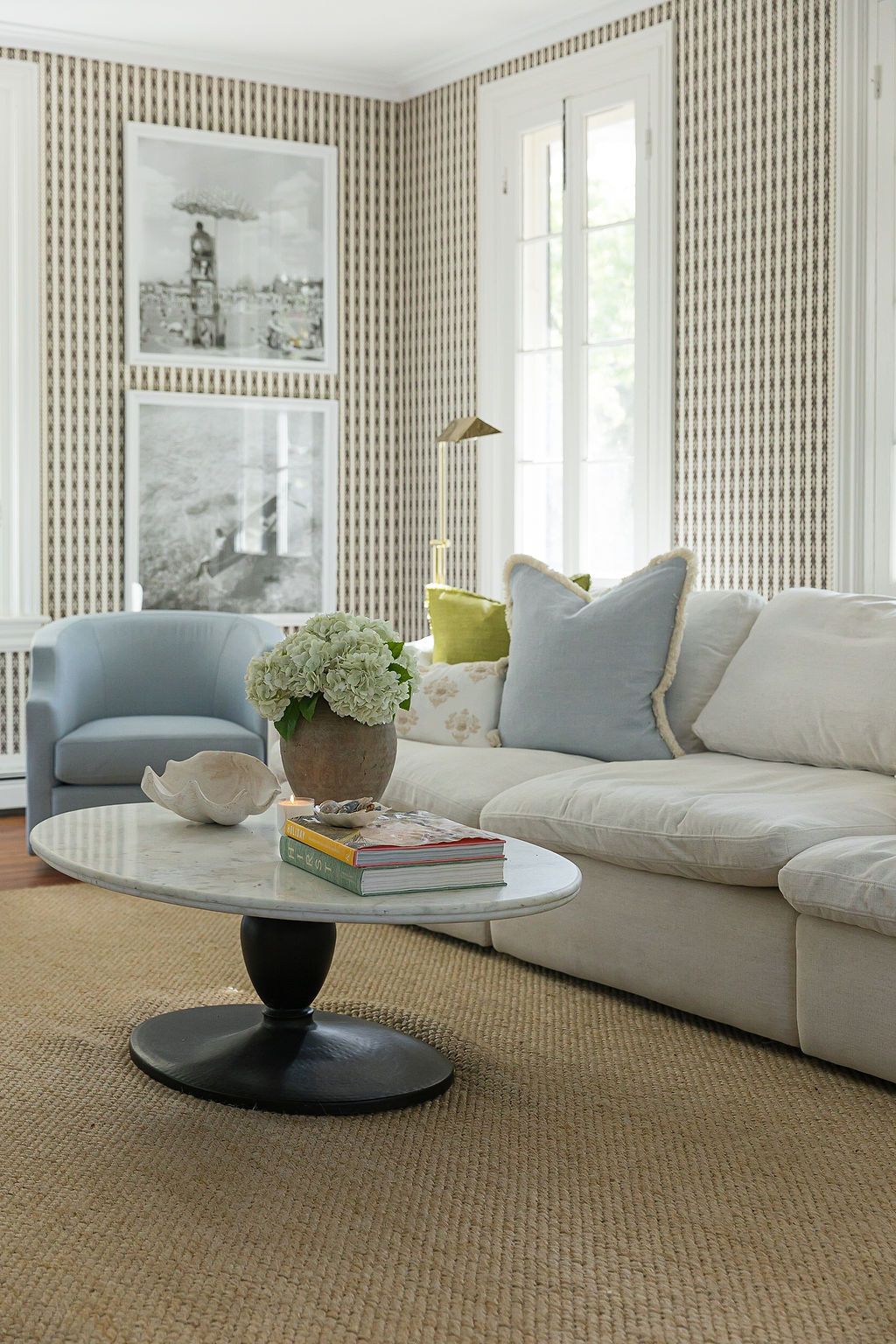 Modern living room interior with textured wallpaper, white sofa, sisal carpet, and round black coffee table.