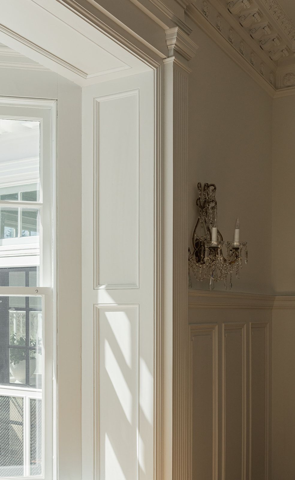 Interior view of an elegant white room with ornate crown molding and a crystal wall sconce.