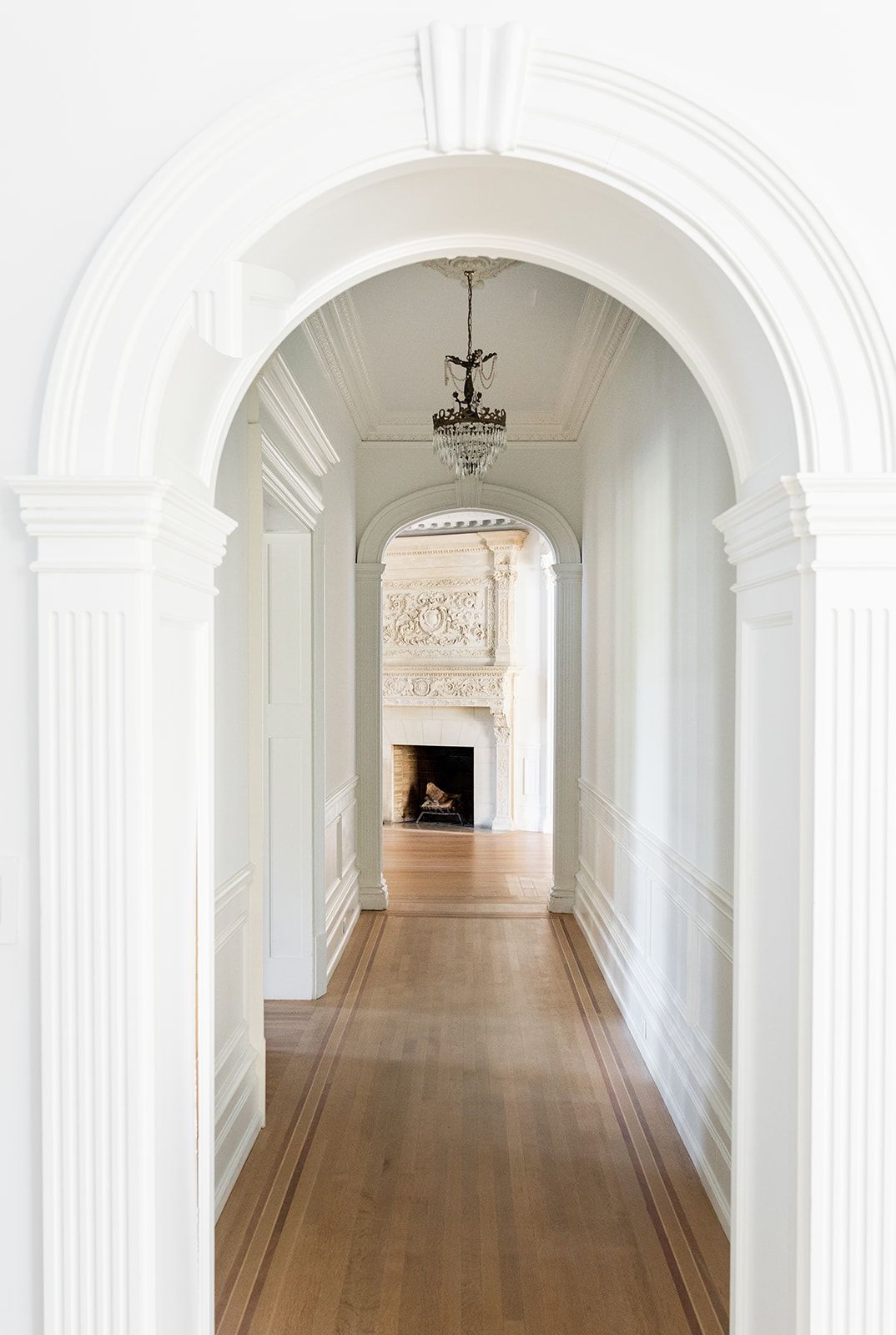 Long white hallway with arched doorways and decorative molding leading to an ornate fireplace.