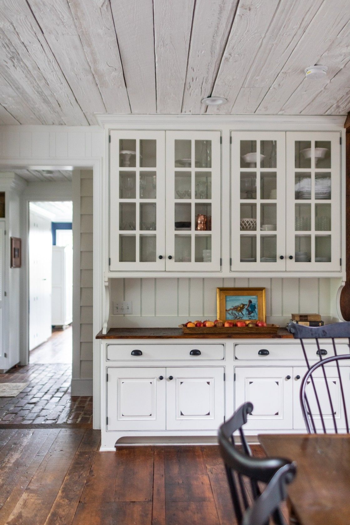Rustic farmhouse kitchen with white glass-front cabinets, butcher block counters, and wide plank wood flooring.