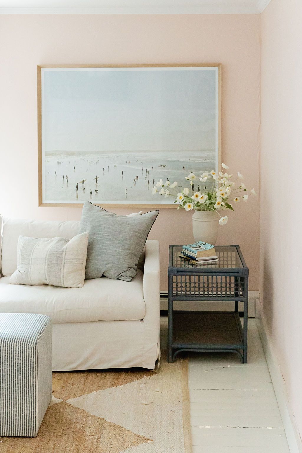 Cozy living room corner with white couch, beachy artwork, and gray accents features a modern side table with vase of flowers.
