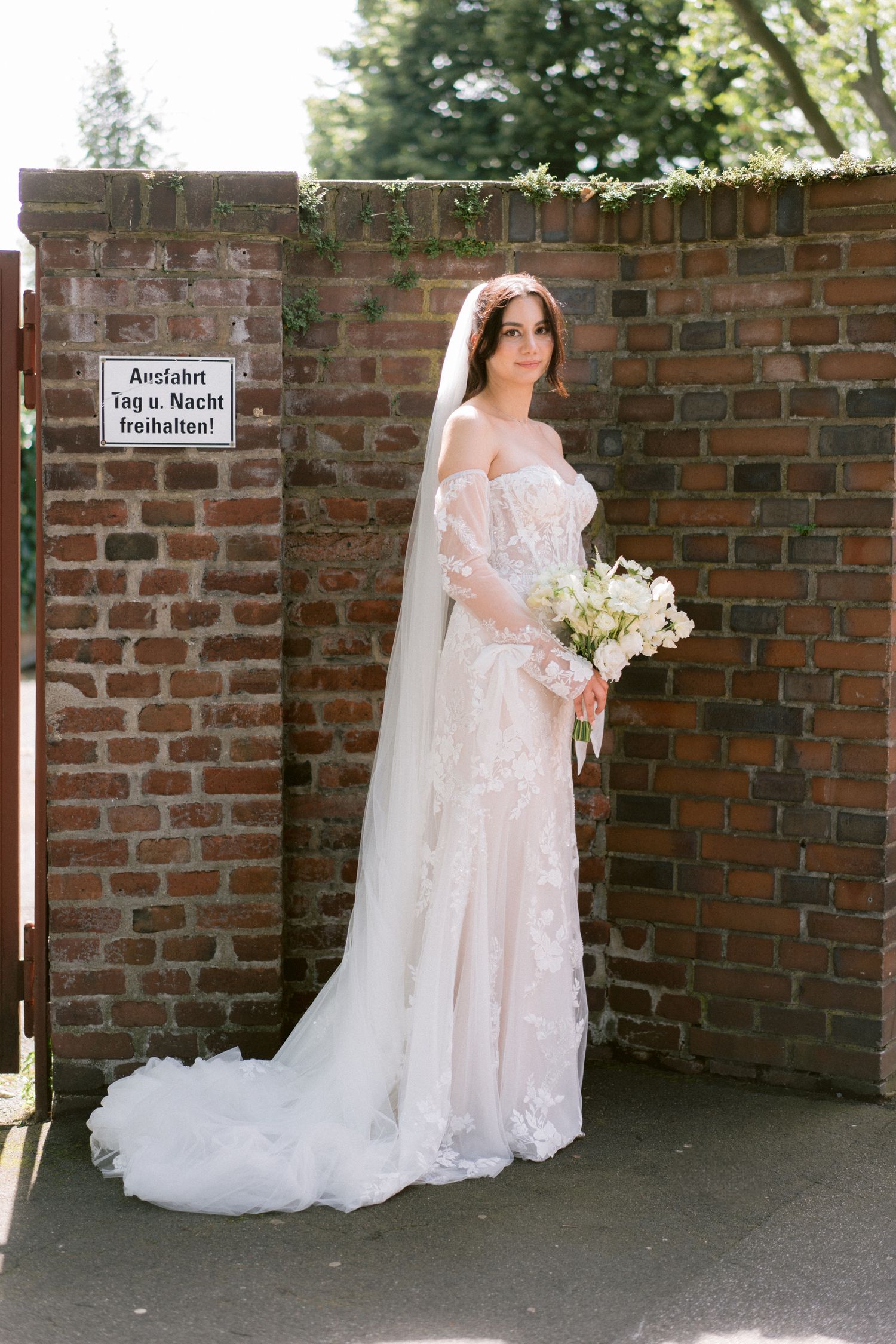 Beautiful lace wedding dress with long train photographed against a brick wall background.