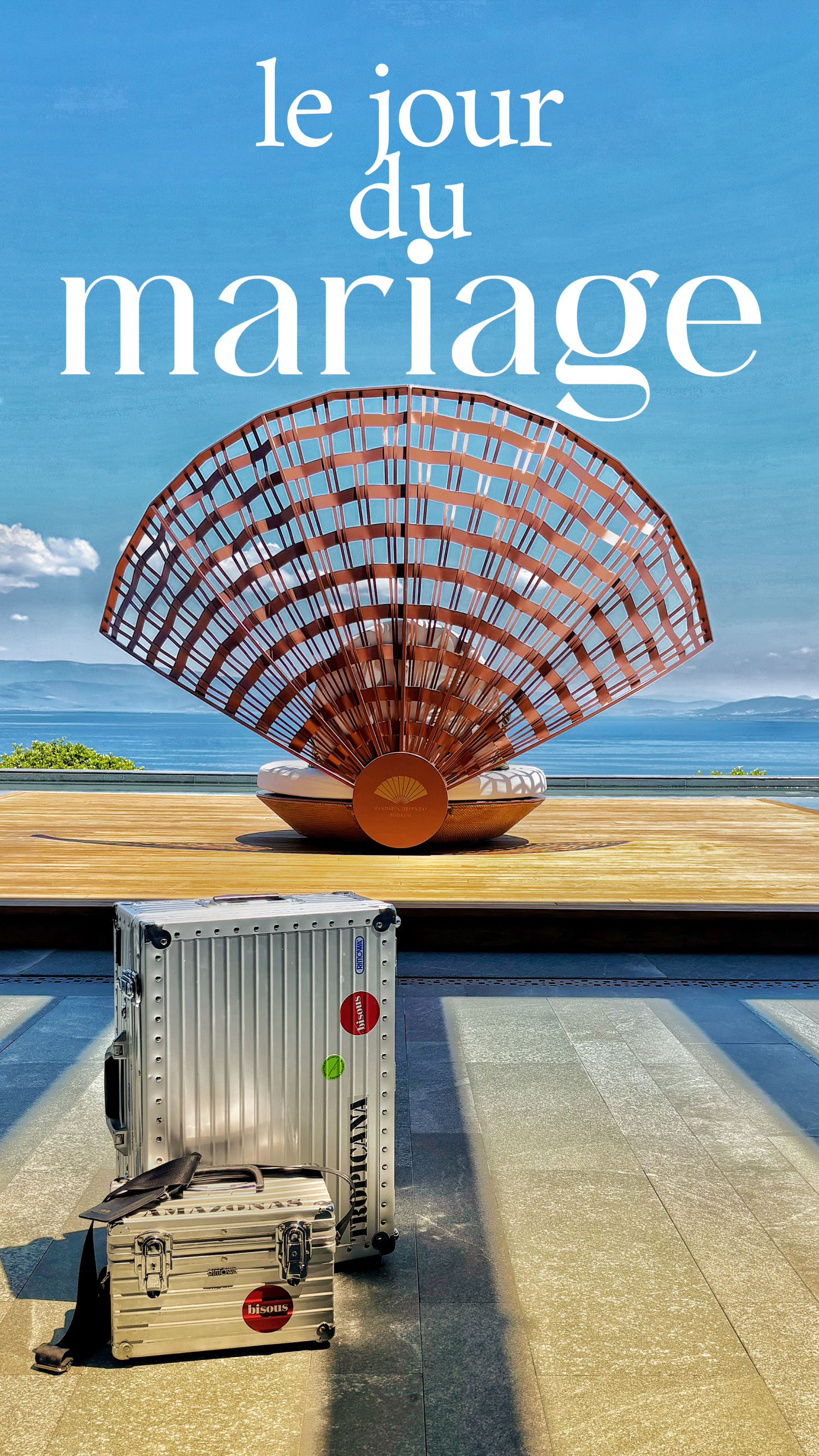 French wedding day scene with silver Rimowa luggage before a fan-shaped sculpture overlooking the sea.