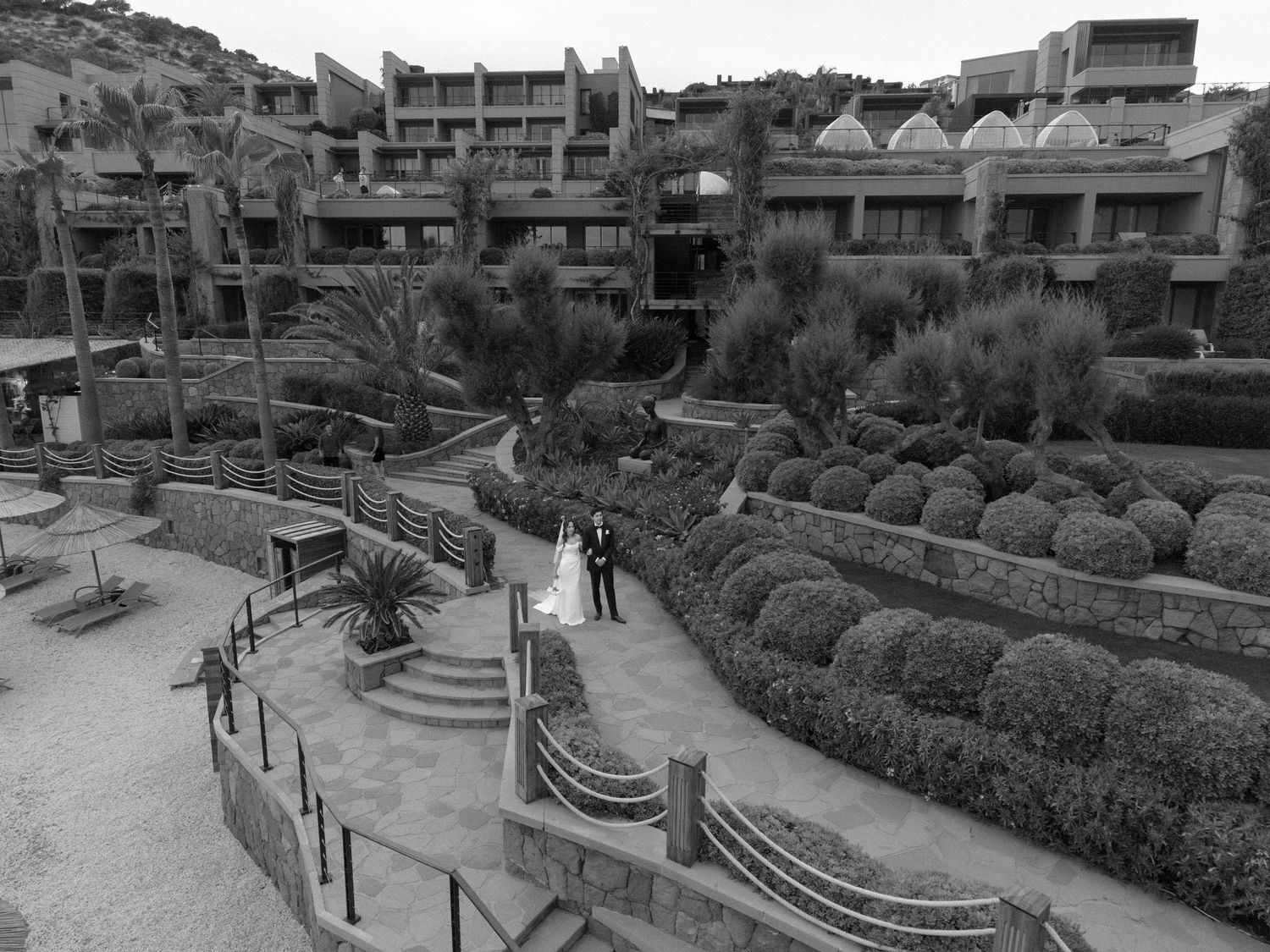 Black and white aerial photo of a wedding couple posing in lush garden terraces outside a luxury resort.