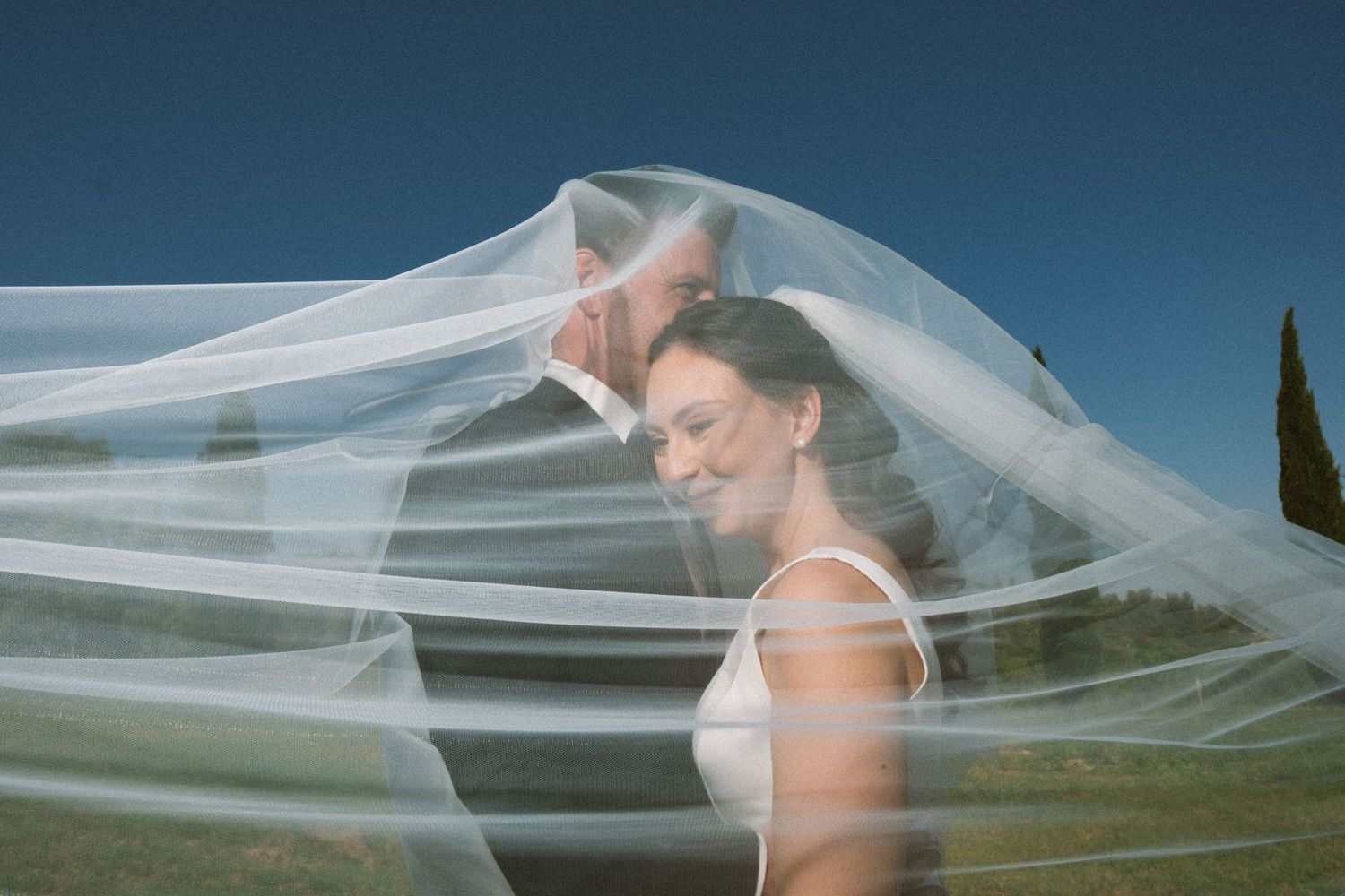 A flowing white wedding veil billows in the breeze against a blue sky backdrop.
