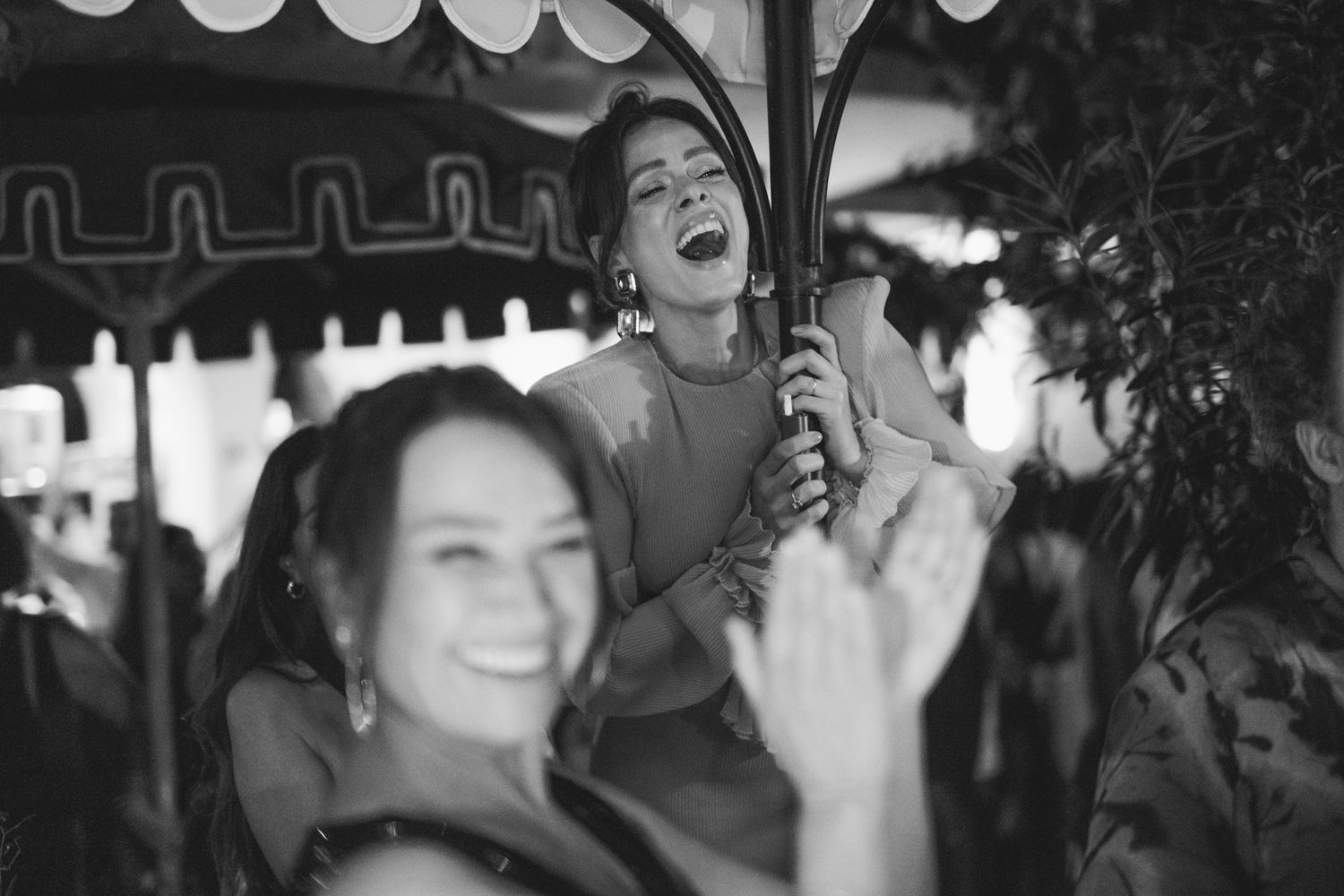 Black and white photo of joyful celebration with people laughing under decorative umbrella.