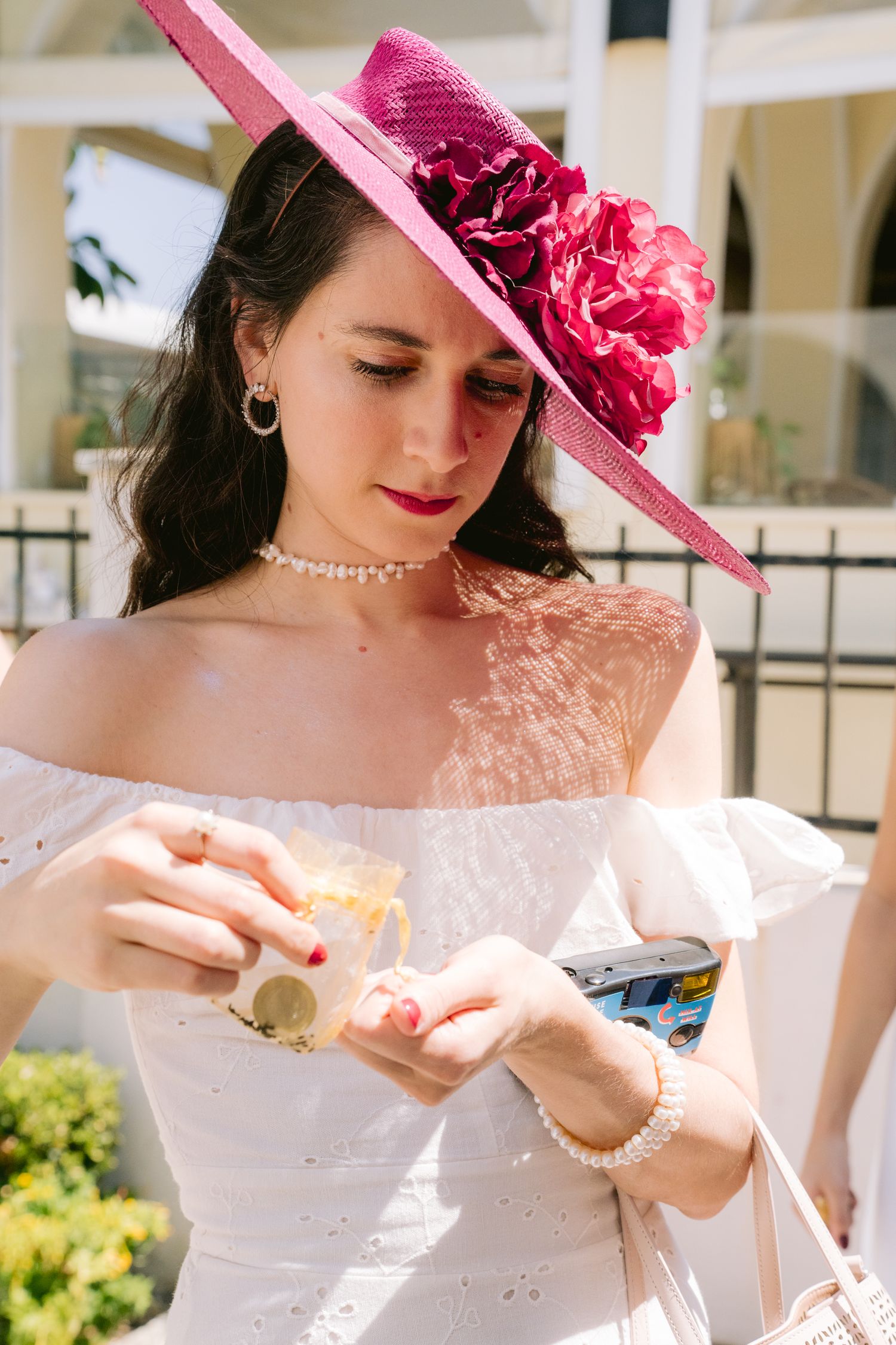 Woman wearing white dress and pink hat delicately handles item at outdoor event.