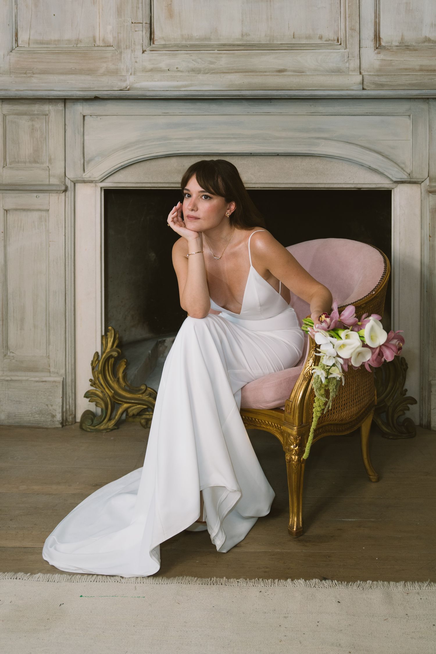 Person in white dress reclining elegantly on vintage gold chaise lounge in classic interior setting.