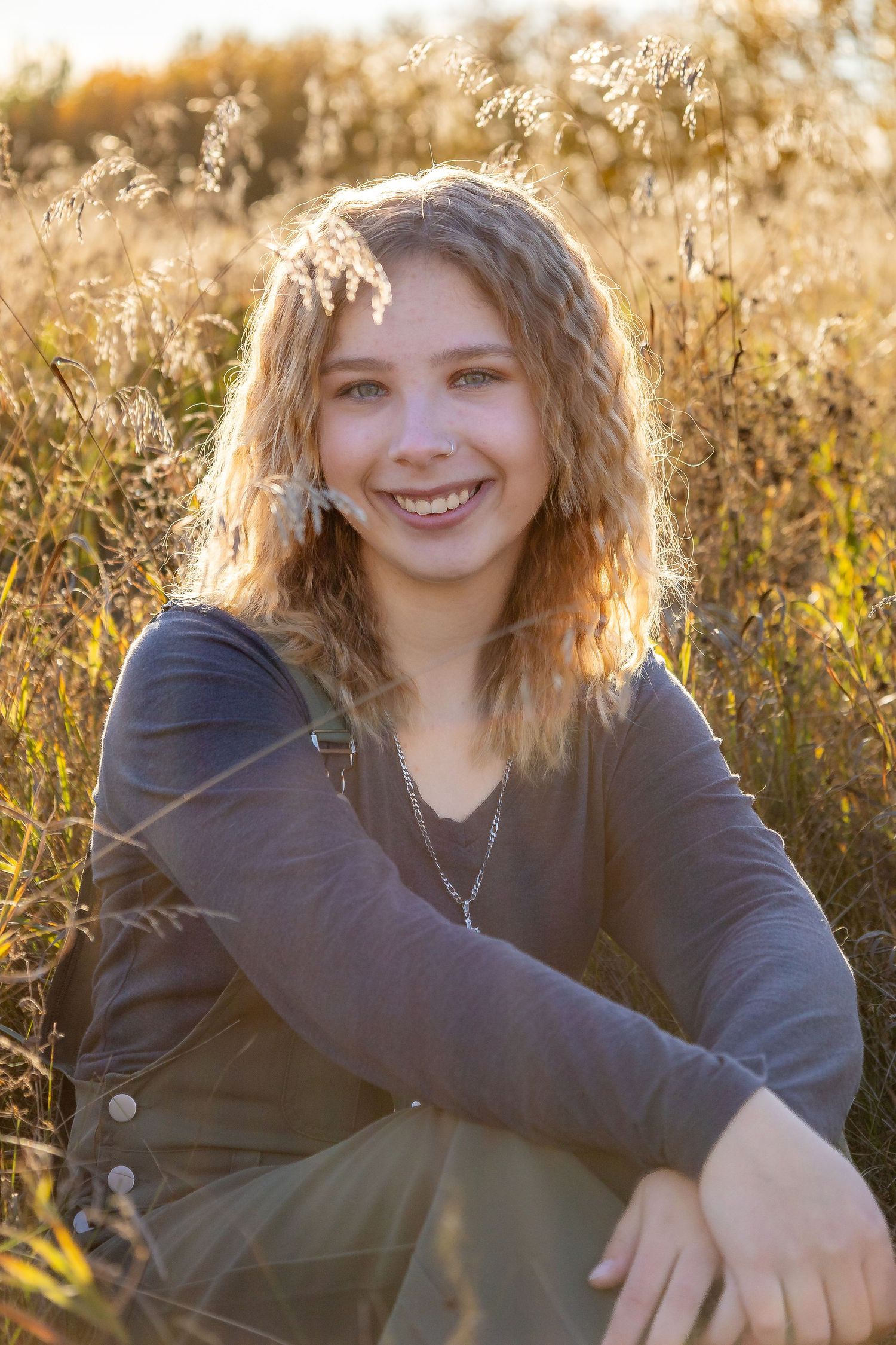 Portrait of young teen smiling in field during golden hour with backlit hair.