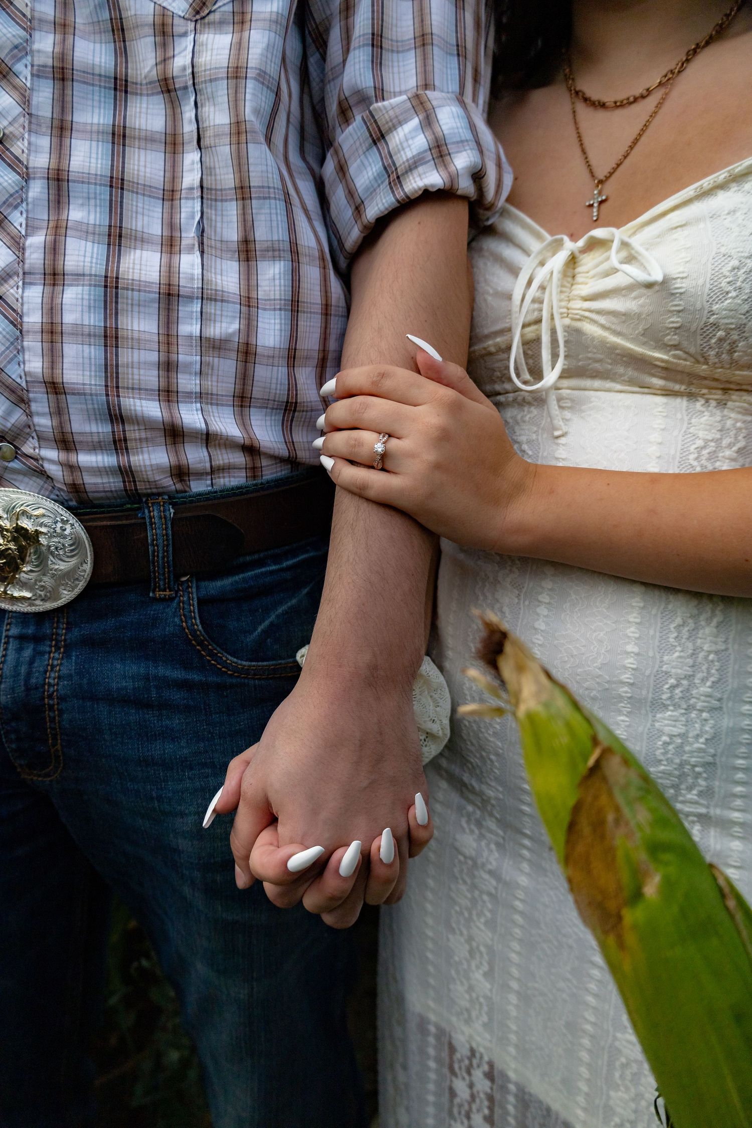 Close-up of couple holding hands showing plaid shirt and white dress details.