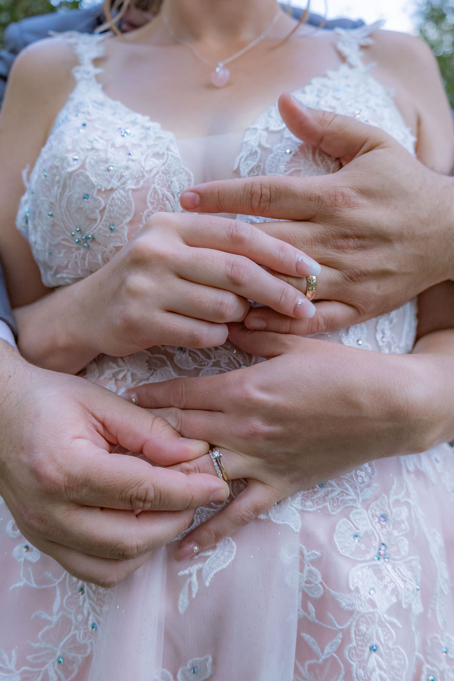 Close-up of hands with wedding rings and delicate lace dress details.