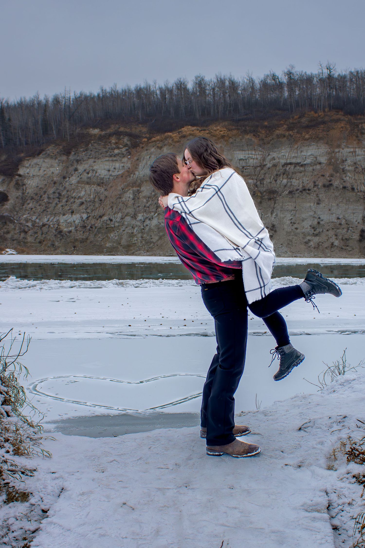Romantic winter embrace against snowy landscape and rocky cliff.