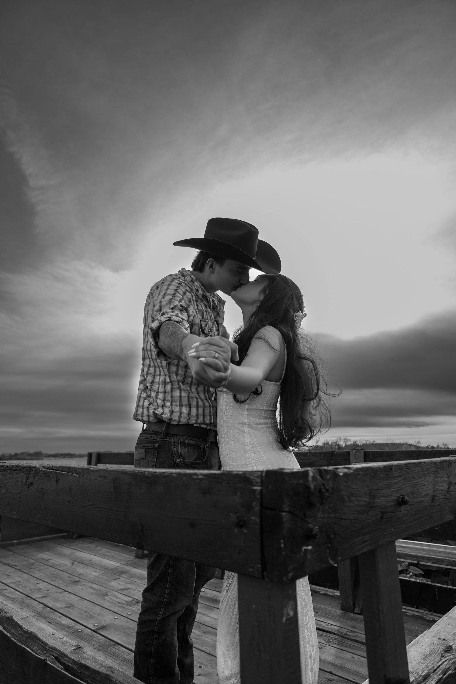 A romantic black and white photo of a couple embracing on a wooden deck at sunset.