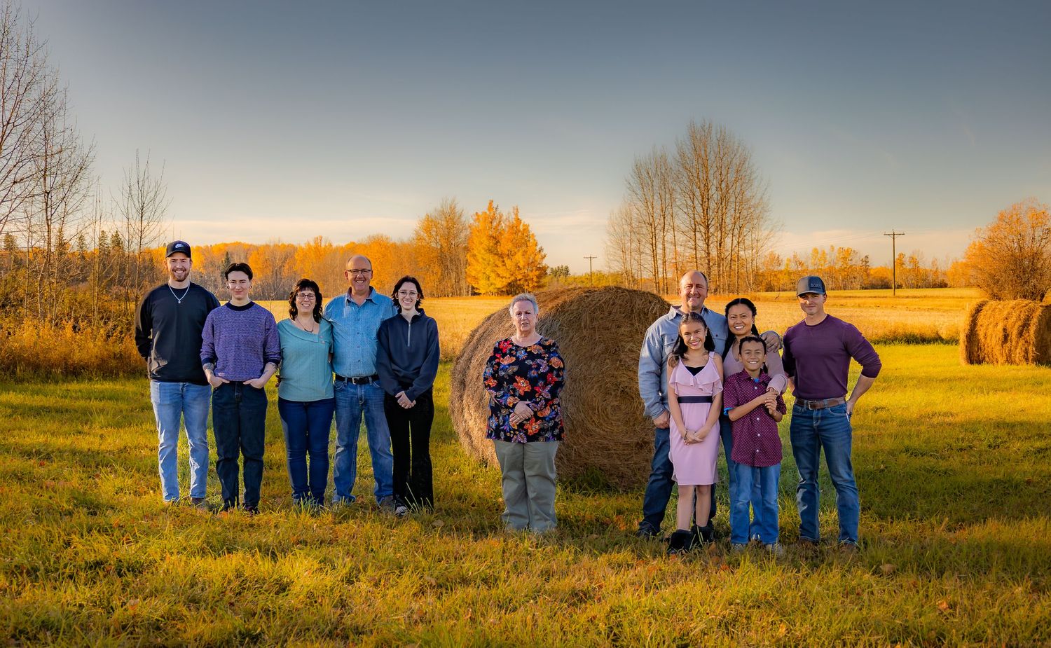 Two families gather for outdoor portrait session near hay bales at sunset.