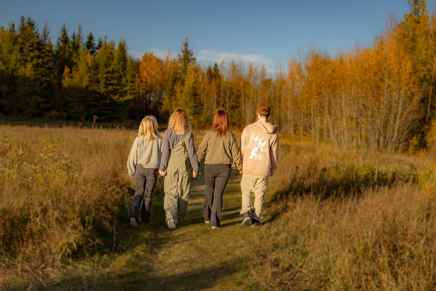 Family walking together through golden autumn field at sunset.