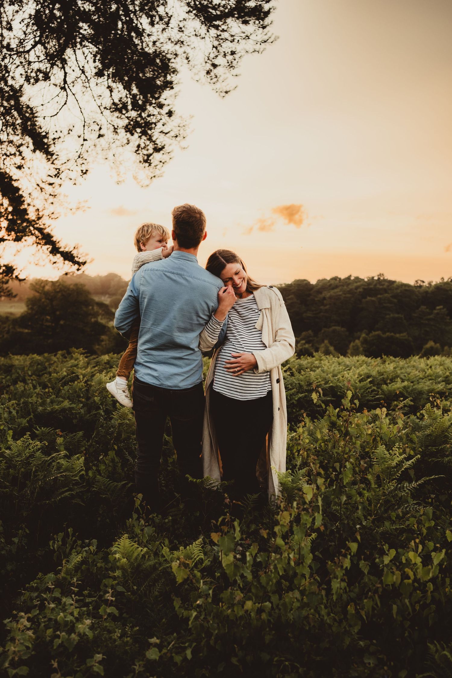 expecting couple with young child standing in a field at sunset during a family maternity photo session near Horsham