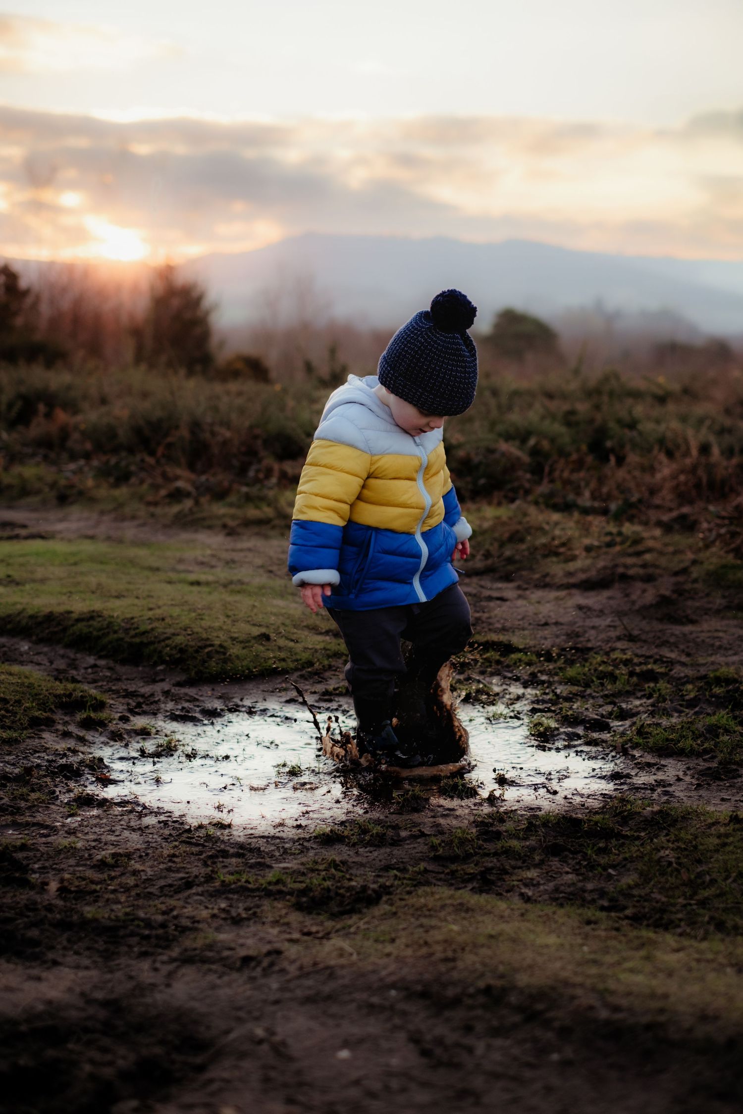 boy jumping in muddy puddle during a playful outdoor photo session in West Sussex South Downs National Park