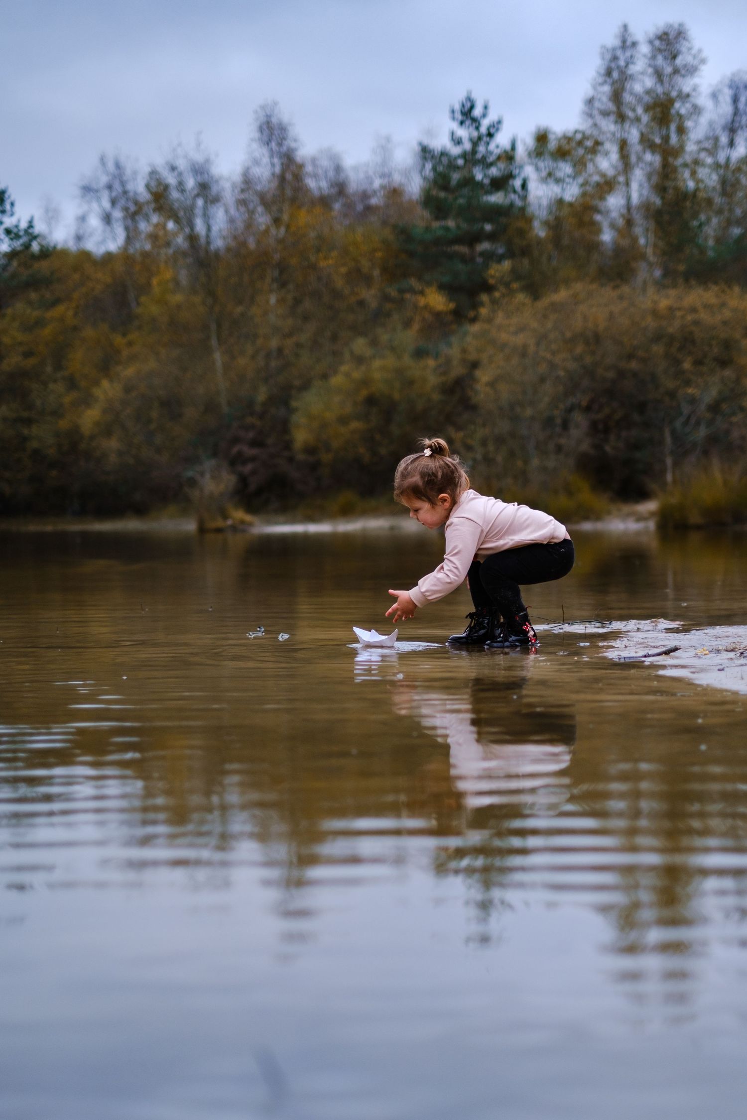 little girl floating a paper boat during an autumn outdoor family session near Midhurst