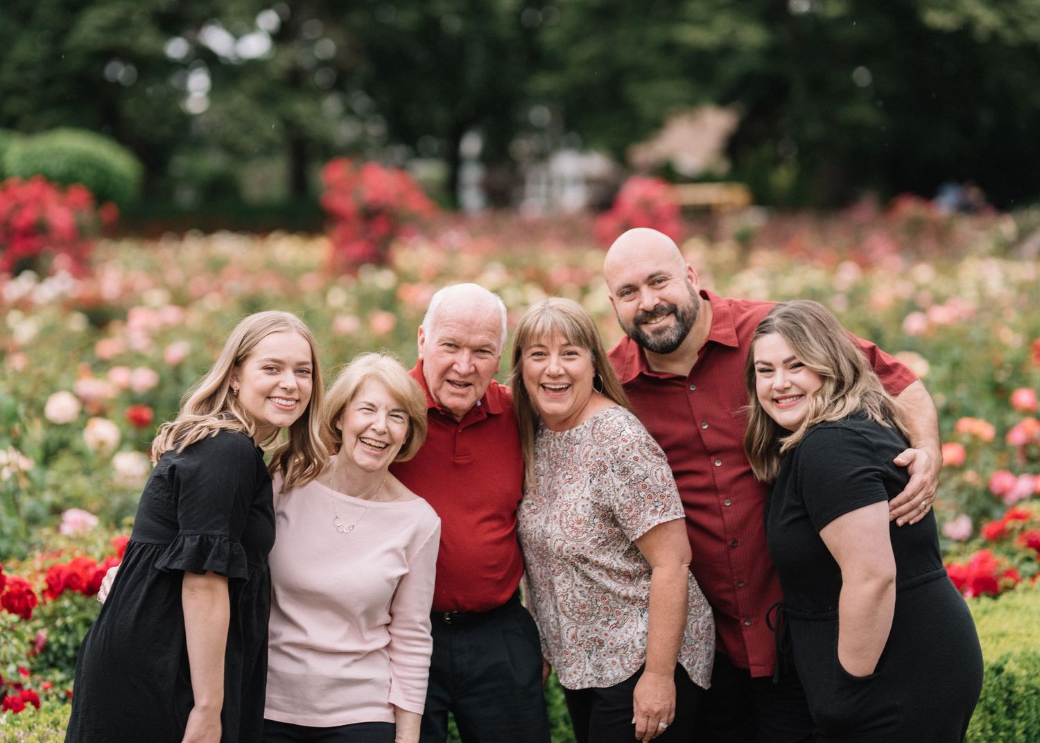 Cheerful group portrait in rose garden with bright flowers in background.