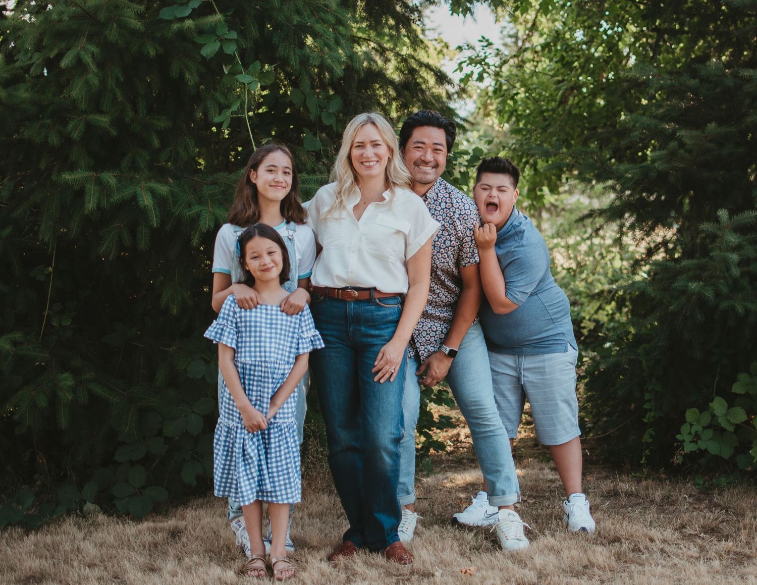 Family of five poses together outdoors in coordinated casual outfits.