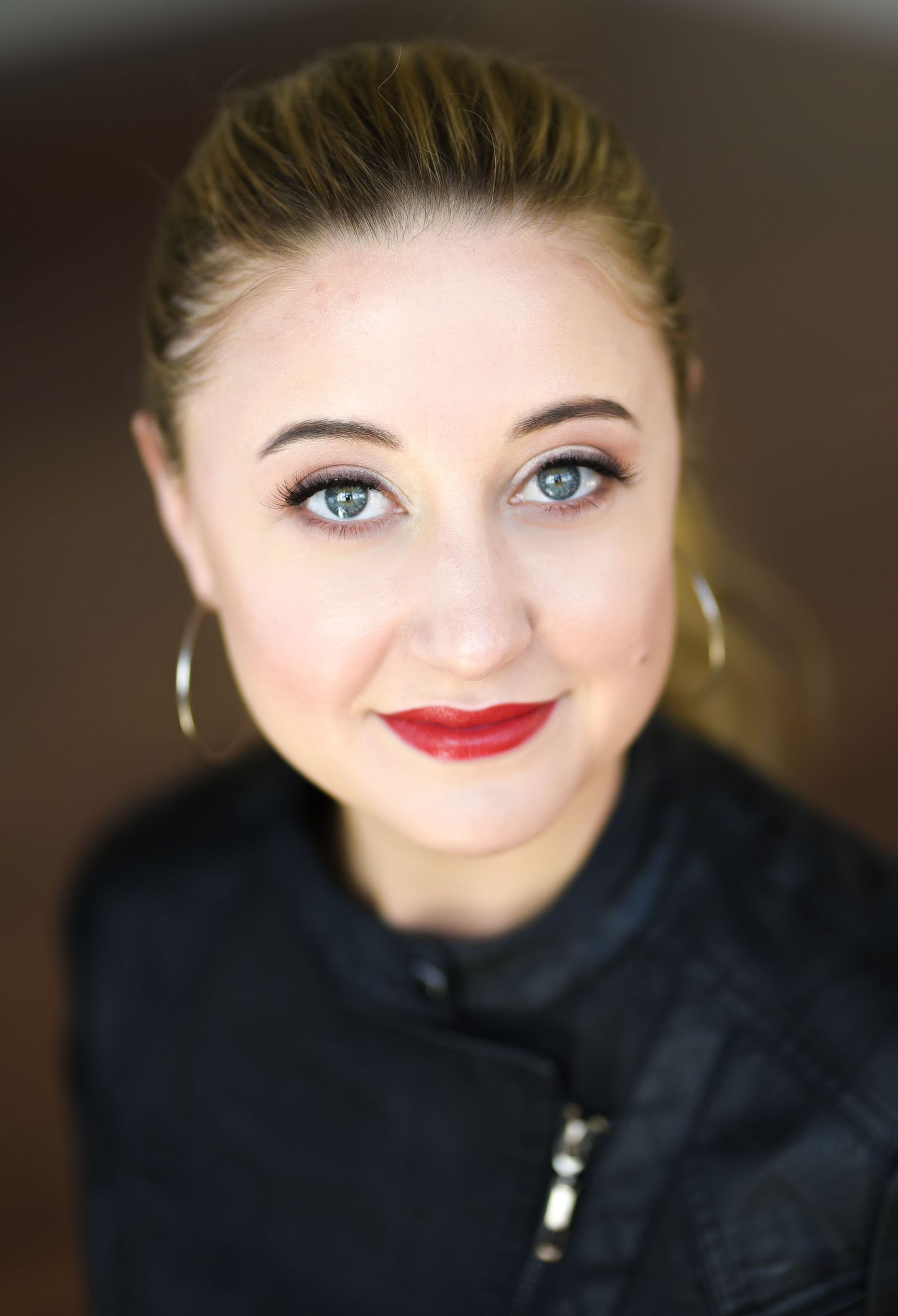 Elegant portrait with red lipstick and gold hoop earrings against a dark background.