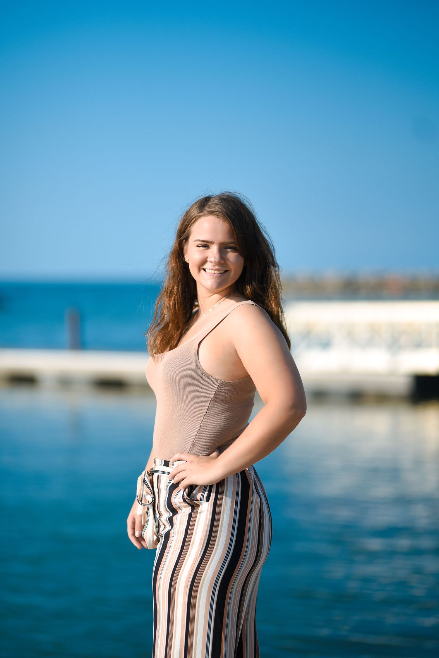 Casual summer portrait by blue ocean water wearing striped pants.