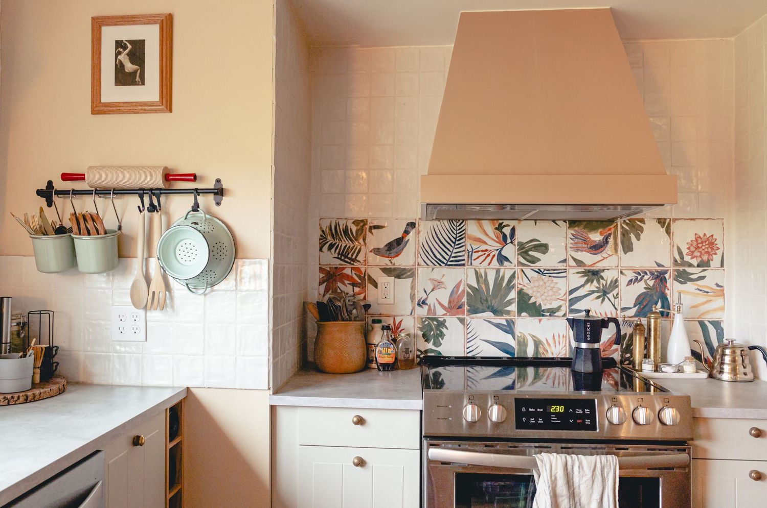 Charming kitchen with floral tile backsplash, hanging utensils, and cream-colored cabinets.