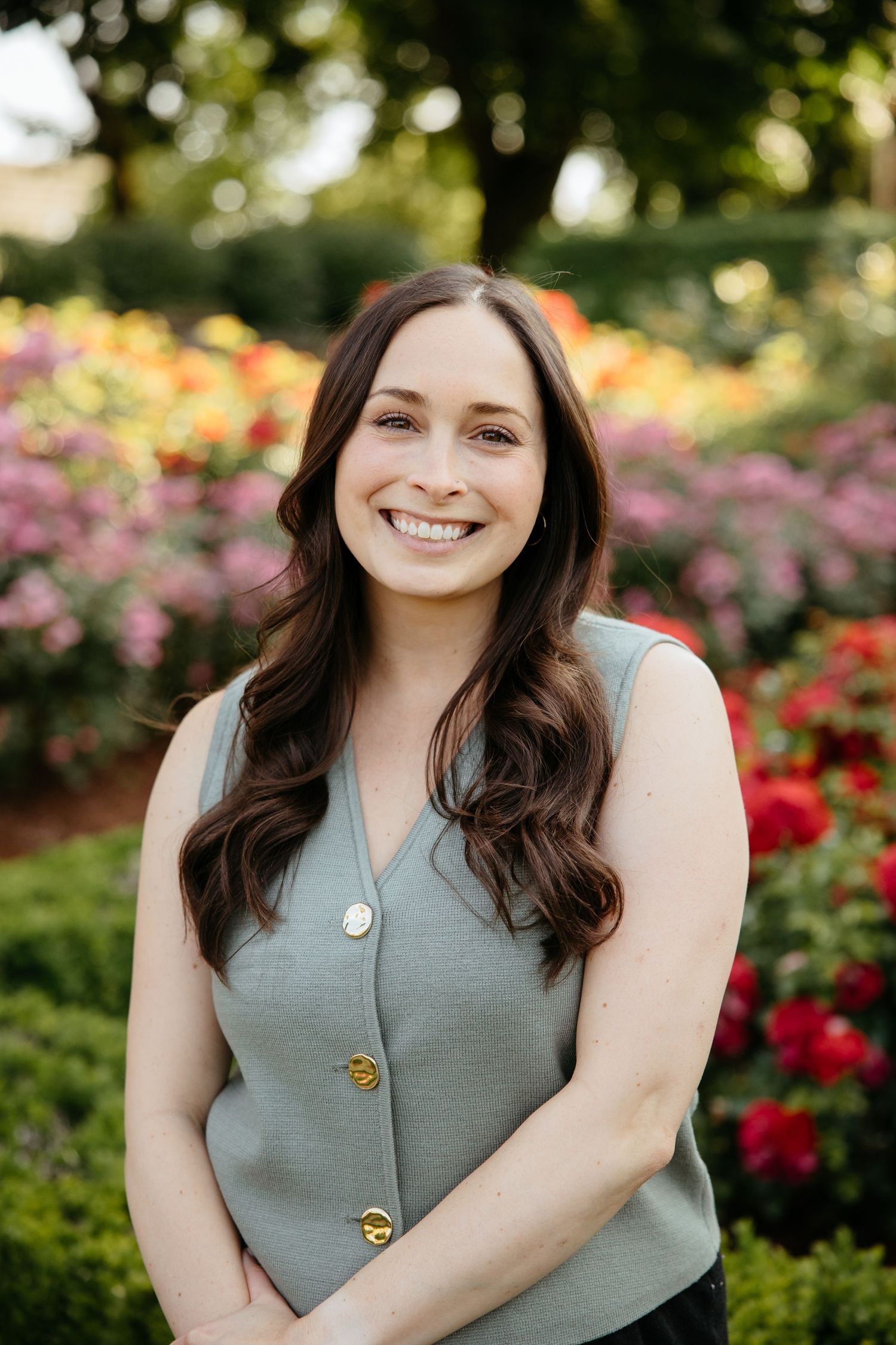 Portrait photo series in a garden with blooming roses featuring someone in a sage green sleeveless top.