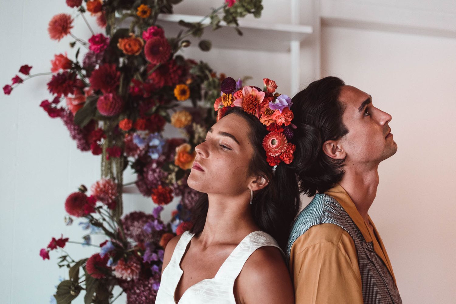 Two people pose playfully with red and burgundy floral arrangements.
